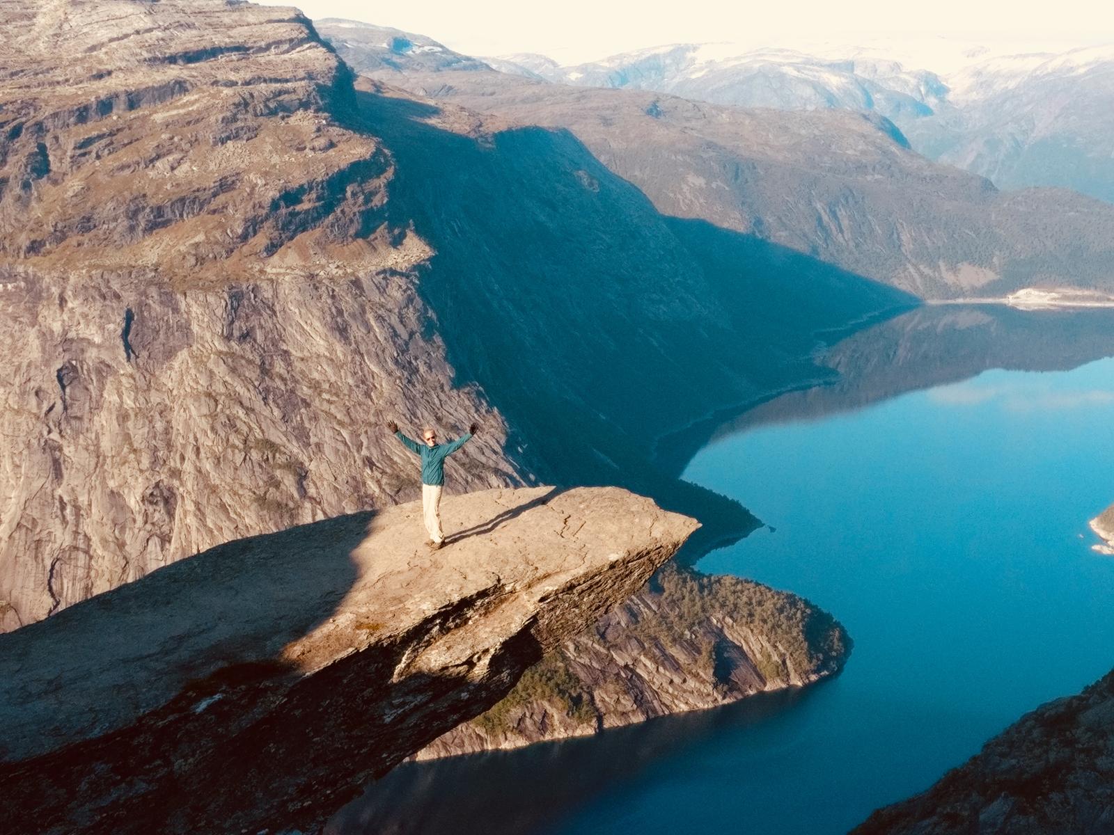 Carol standing triumphantly on a cliff above a deep blue fjord